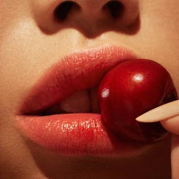 Close-up of a person with glossy lips about to bite a cherry, highlighting lip makeup and nail art ideal for shopping inspiration