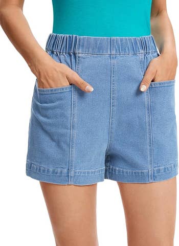 Close-up of a person wearing high-waisted denim shorts with pockets. The person is wearing a top, hands in pockets