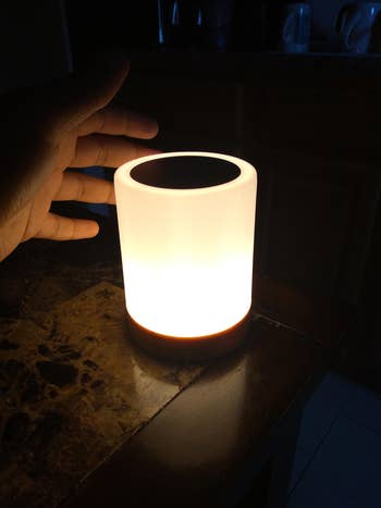 reviewer's hand reaching towards a illuminated portable lamp on a countertop