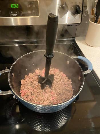 reviewer's beef cooking in a pot with the heat-resistant masher in the center