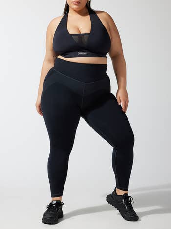 Plus-size model in black athleisure wear, including a sports bra and leggings, paired with black sneakers, showcasing a shopping category for activewear