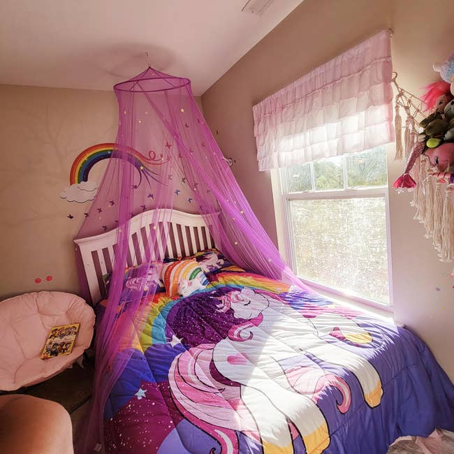 child's bed with a purple canopy with gold stars on it hanging above