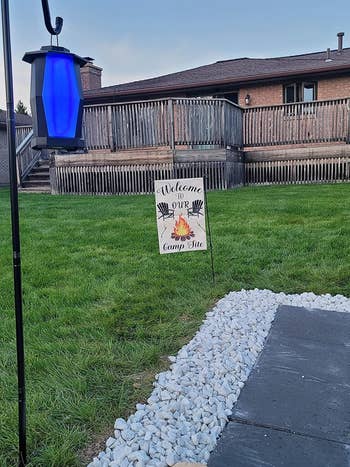 The lantern speaker hanging from a pole in a reviewer's yard while it lights up in a blue color