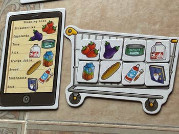Shopping list on a tablet and a magnetic toy shopping cart. Items listed and shown: strawberries, eggplants, tuna, milk, orange juice, bread, toothpaste, book