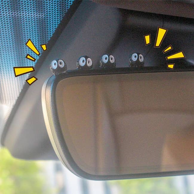 Cute, small decorations with googly eyes sit atop a car's rearview mirror,