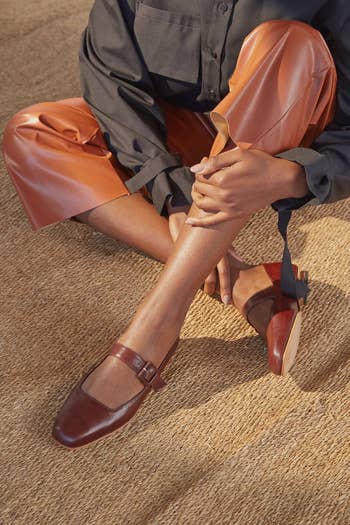 Person seated wearing brown loafers with black soles and tan trousers. Hands clasped over one knee