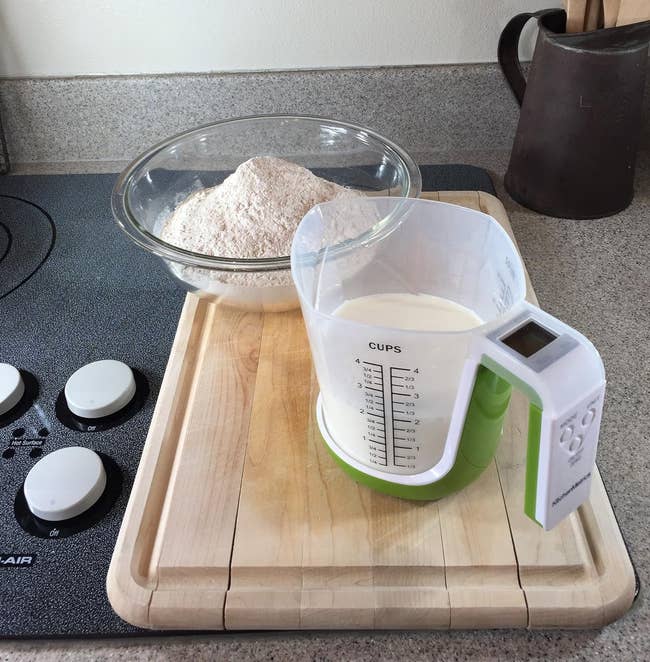 A clear plastic measuring cup resting on a handled digital white and green scale 