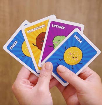 Hands holding four animated food-themed cards labeled 