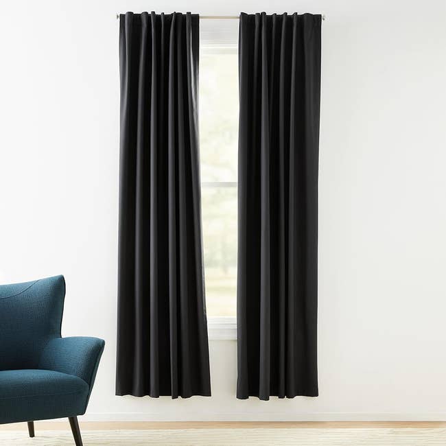 Black curtains hang on a window beside a blue armchair in a bright room