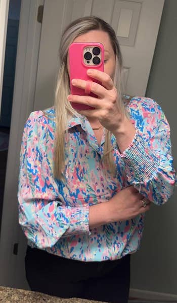 Reviewer taking a mirror selfie in a colorful patterned blouse and black pants