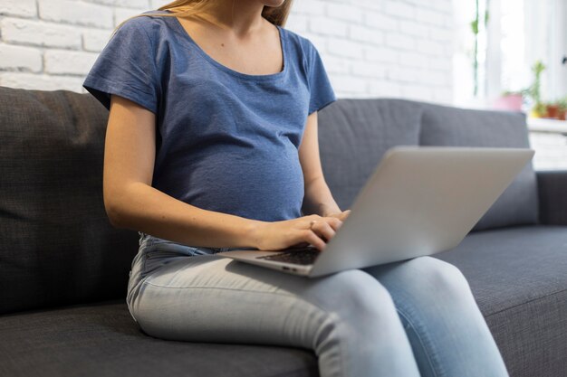 Ciężarna bizneswoman siedzi na kanapie i pracuje na laptopie