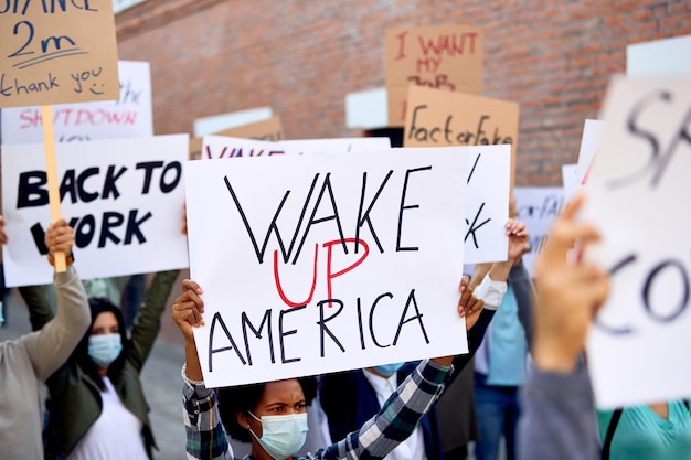 Duża grupa demonstrantów demonstrujących na ulicach USA Koncentruje się na czarnej kobiecie trzymającej znak „Obudź się Amerykanin”