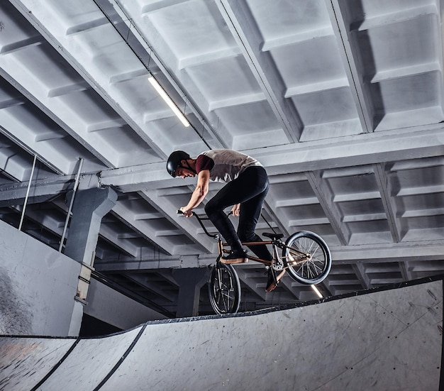 Bezpłatne zdjęcie freestyle bmx. młody bmx robi sztuczki na swoim rowerze w skateparku pod dachem