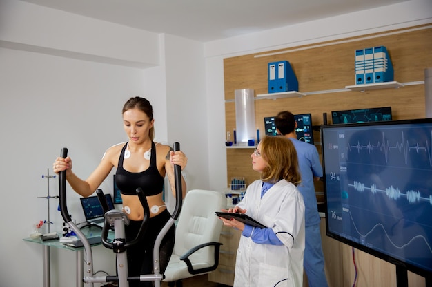 Bezpłatne zdjęcie lekkoatletka robi wysiłek fizyczny na stepperze, a lekarz podąża za nią. laboratorium sportowe