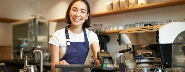 Bezpłatne zdjęcie mały biznes i uśmiechnięci ludzie azjatycka barista pracująca w kawiarni dająca kredyt na terminalu