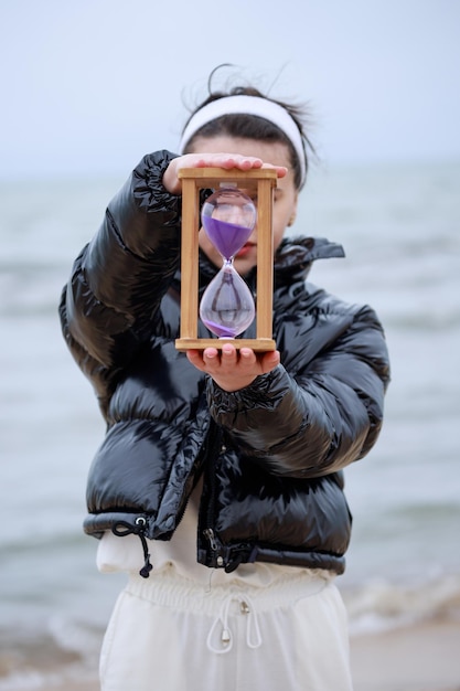 Bezpłatne zdjęcie młoda kobieta trzyma zegar z piaskiem na plaży zdjęcie wysokiej jakości