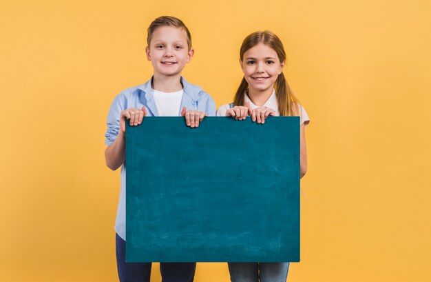 Portret chłopiec i dziewczyny mienia zieleni chalkboard pozycja przeciw żółtemu tłu