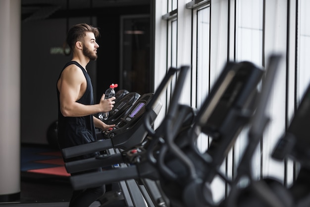 Bezpłatne zdjęcie portret młodego sportowca wykonującego trening cardio i wodę pitną na siłowni