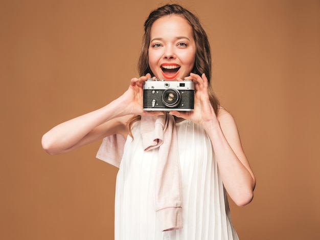 Bezpłatne zdjęcie portret rozochocona młoda kobieta bierze fotografię z inspiracją i jest ubranym biel suknię. dziewczyna trzyma aparat retro. pozowanie modelu