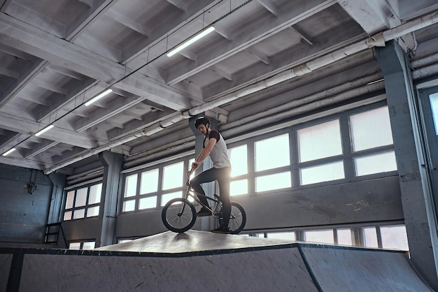 Bezpłatne zdjęcie profesjonalny zawodnik bmx w kasku ochronnym, przygotowujący się do skoku w skateparku w pomieszczeniu