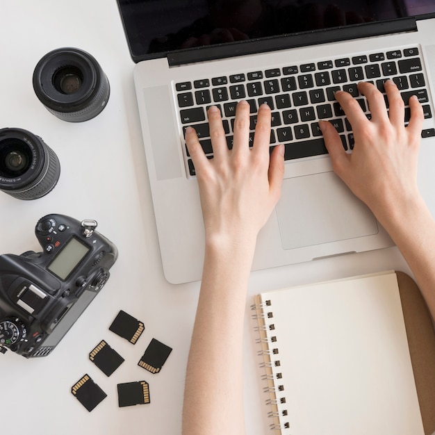 Bezpłatne zdjęcie ręka osoby pisania na klawiaturze laptopa z akcesoriami aparatu i książki spirali