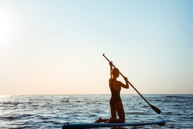 Bezpłatne zdjęcie sylwetka młody piękny kobieta surfing w morzu przy wschodem słońca.