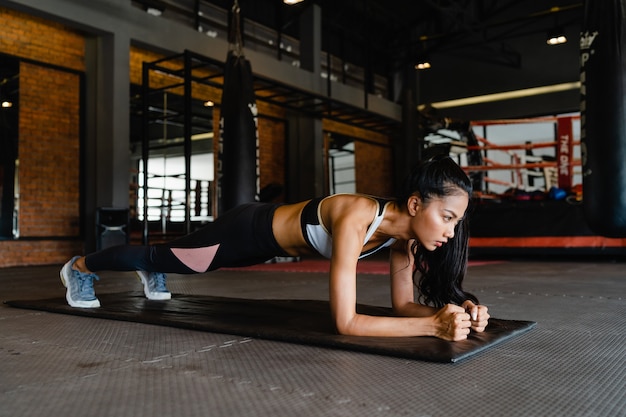 Szczęśliwa młoda azjatycka dama robi trening spalania tłuszczu deski w klasie fitness.