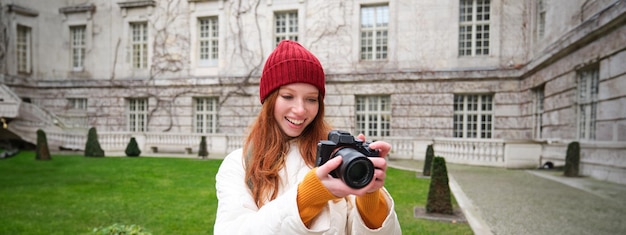 Bezpłatne zdjęcie szczęśliwa rudowłosa turystka robi zdjęcia fotografowi z profesjonalnym aparatem spacerując po mieście i