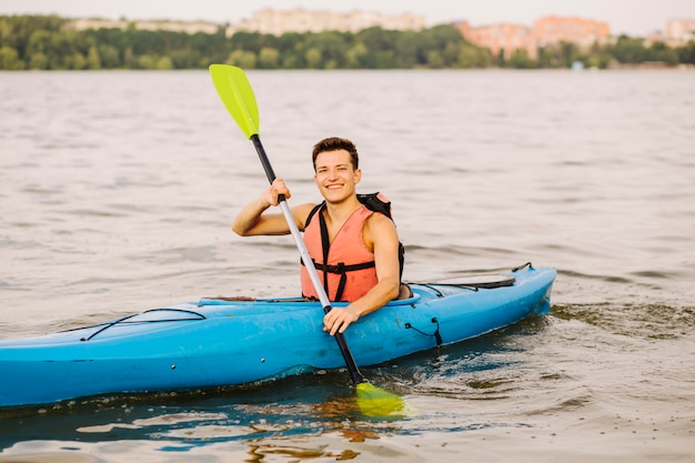 Bezpłatne zdjęcie szczęśliwy młody człowiek używa paddle kayaking na jeziorze