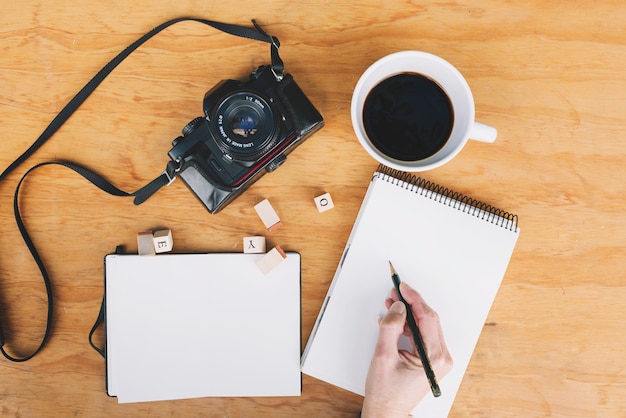 Bezpłatne zdjęcie uprawy ręki writing w notatniku blisko kamery i kawy