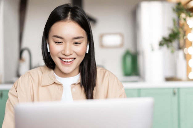 Bezpłatne zdjęcie uśmiechnięta azjatka słucha oglądając na laptopie patrząc na komputer podczas webinaru online koncepcja...