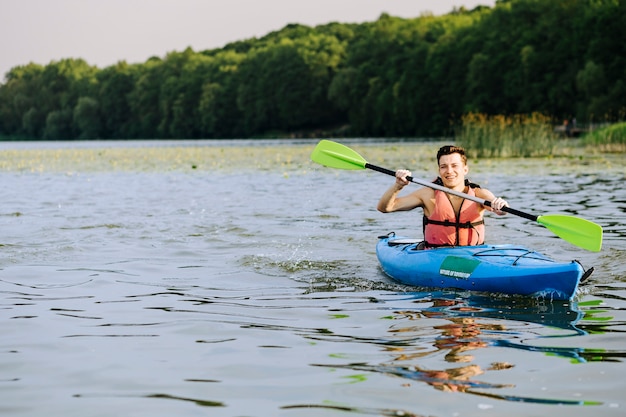 Bezpłatne zdjęcie uśmiechnięta mężczyzna chełbotania woda podczas gdy paddling kajak na jeziorze