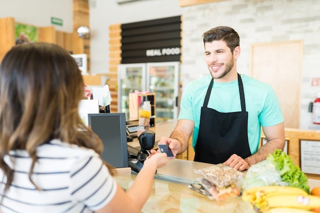 Bezpłatne zdjęcie uśmiechnięty mężczyzna kasjer odbierający płatność kartą kredytową w supermarkecie