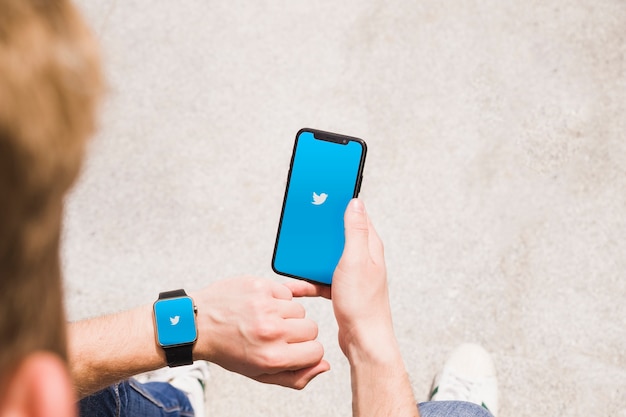 Bezpłatne zdjęcie zakończenie mężczyzna z smartwatch i telefonem komórkowym pokazuje twitter app