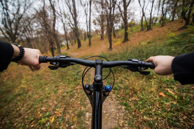 Bezpłatne zdjęcie zakończenie wizerunek cyklisty mężczyzna ręki na kierownicy jeździeckim rowerze górskim na śladzie w jesień parku