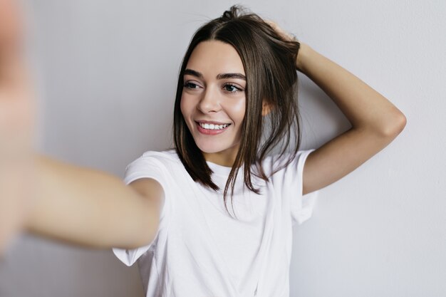 Bella donna abbronzata con gli occhi marroni che fa selfie e che ride. signora elegante isolata.