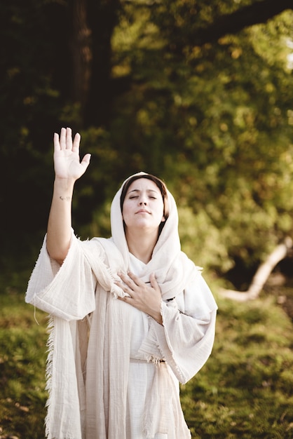 Foto gratuito colpo verticale della femmina che indossa un abito biblico con le mani in alto verso il cielo pregando