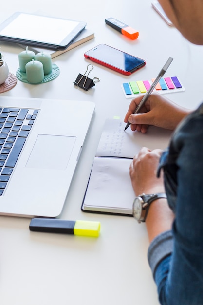 Donna che scrive in taccuino sul tavolo con computer portatile e attrezzature