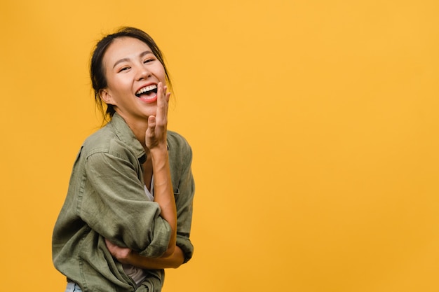 Foto gratuito giovane signora asiatica con un'espressione positiva, sorride ampiamente, vestita con abiti casual sul muro giallo. la donna felice adorabile felice si rallegra del successo. concetto di espressione facciale.