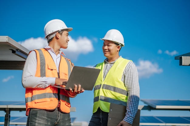 Foto gratuito giovane tecnico asiatico e collega in uniforme di sicurezza che controllano il funzionamento del sole e del pannello solare fotovoltaico e utilizzano il computer portatile mentre si lavora nella fattoria solare