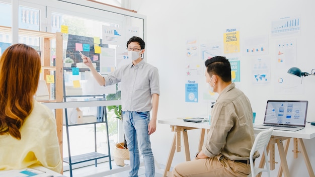 Foto gratuito gli imprenditori asiatici che incontrano idee per il brainstorming conducono idee per presentazioni aziendali proiettano colleghi e indossano una maschera protettiva nel nuovo ufficio normale. stile di vita e lavoro dopo il coronavirus.