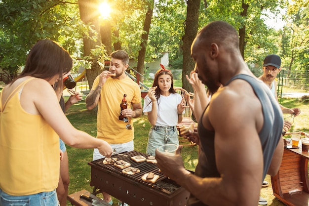 Foto gratuito gruppo di amici felici che hanno birra e barbecue party in giornata di sole. riposare insieme all'aperto in una radura della foresta o in un cortile