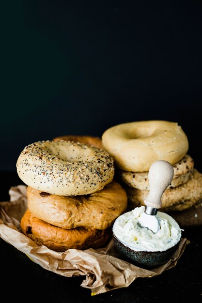 Impilati di diversi tipi di bagel con formaggio nella ciotola contro sfondo nero