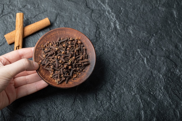 Foto gratuito mano che tiene un piatto marrone con chiodi di garofano secchi.