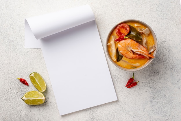 Foto gratuito minestra piatta laica in una ciotola con gamberi limone e taccuino in bianco