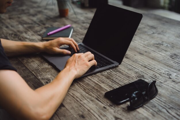 portatile su un tavolo di legno, le mani di un uomo che lavora su un computer