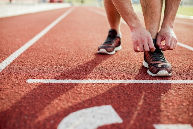 Foto gratuito primo piano della giovane donna che lega la scarpa di sport sulla pista di corsa rossa