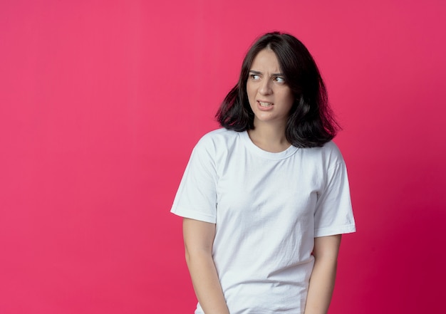 Foto gratuito ragazza abbastanza caucasica giovane infastidita che esamina lato isolato su fondo cremisi con lo spazio della copia