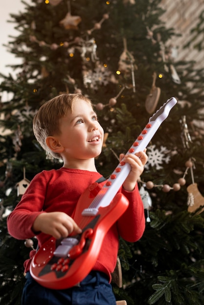 Ragazzino che tiene una chitarra accanto all'albero