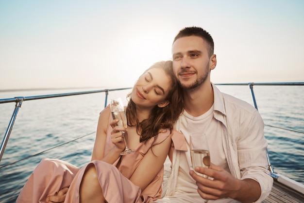 Ritratto all'aperto del maschio e della femmina felici adulti nell'amore, celebrando il loro impegno sull'yacht, tenendo vetro di champagne e abbracciare. Il ragazzo ha appena parlato delle cose che gli piacciono